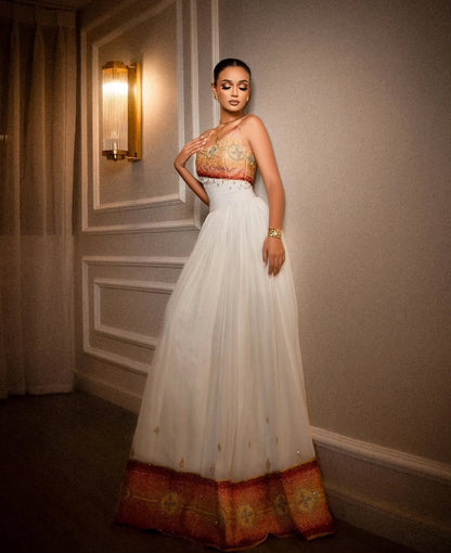 A woman wearing a strapless white tulle Habesha Dress  with an ornate gold and red embroidered bodice, posing against a gray paneled wall.