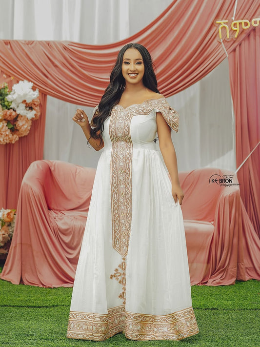 Woman in a white and gold Gold Habesha Kemis standing in front of pink draped curtains.