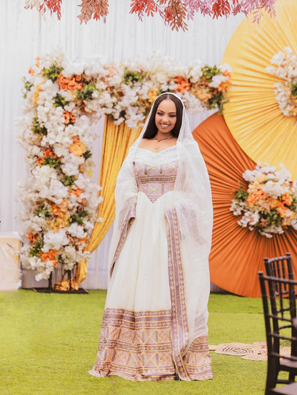 Woman in a traditional outfit standing in front of decorative floral arrangements and a yellow circular backdrop.