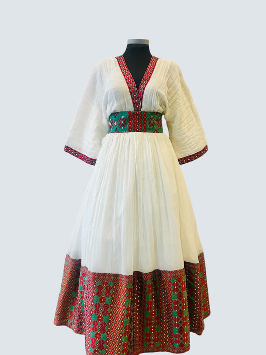 A white cotton maxi Ethiopian Outfit with red and green patterned borders, displayed on a black mannequin against a light gray background.