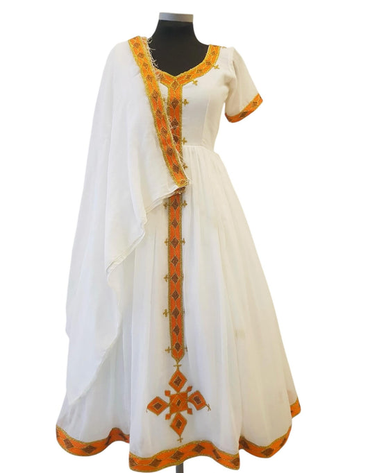 A white traditional Ethiopian Outfit displayed on a black mannequin against a plain white background. The dress features orange and green embroidered borders, a matching draped scarf, and a flared skirt.