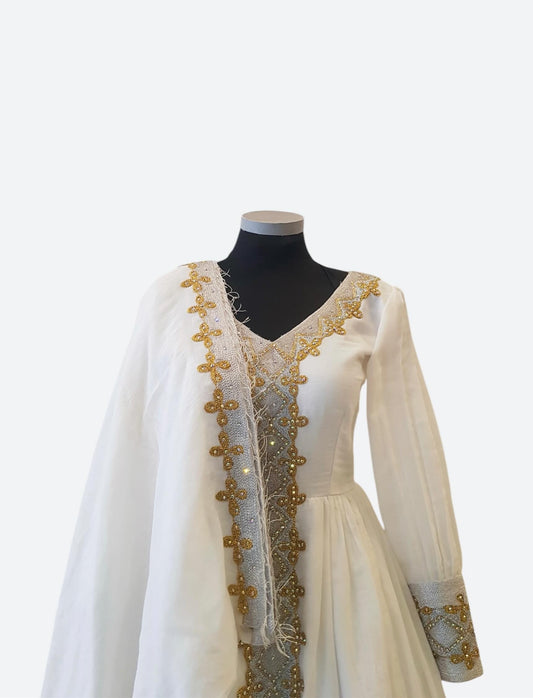 An off-white traditional Ethiopian Outfit displayed on a black mannequin torso, featuring gold and silver beadwork and embroidery along the neckline, front opening, and cuffs.