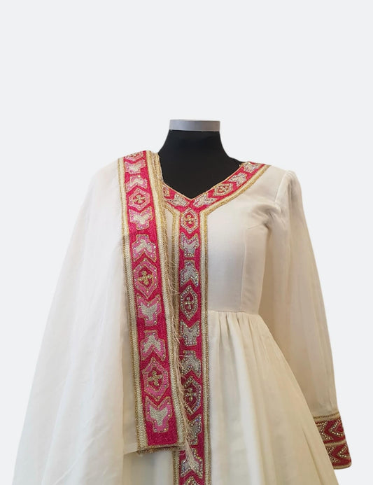 An off-white traditional Ethiopian Outfit  displayed on a black mannequin torso, featuring a vibrant pink and gold embroidered border down the front and along the sleeve cuffs.