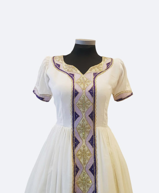 A cream-colored Ethiopian Outfit  displayed on a black mannequin torso, featuring short sleeves, a V-neckline, and ornate vertical embroidery with purple and gold geometric patterns.