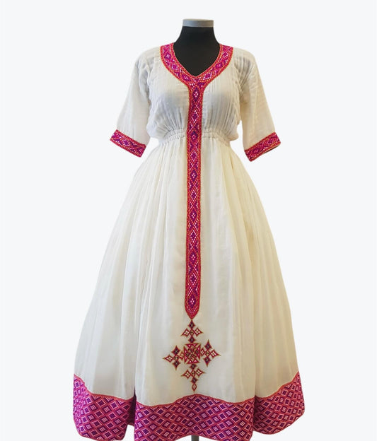 A white A-line Ethiopian Outfit  displayed on a black mannequin against a light gray background. The dress features vibrant magenta pink geometric embroidery along the V-neckline, sleeve cuffs, and hem, with a matching vertical embroidered panel on the front and a decorative cross motif near the bottom.