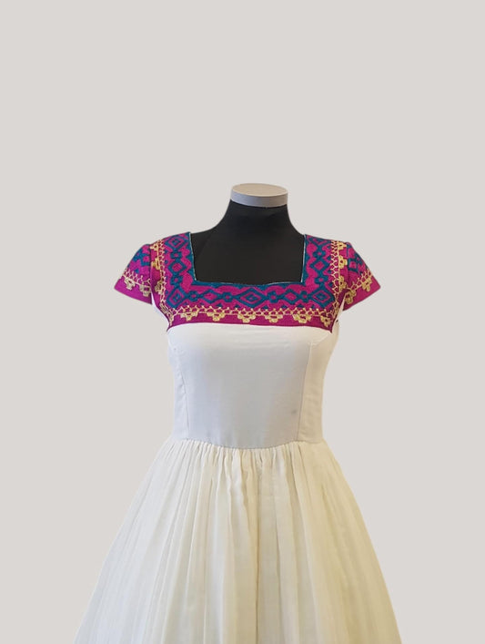 A white Ethiopian outfit displayed on a black against a light gray background. The dress features a white skirt and a square neckline with colorful embroidered trim in pink, purple, and gold.