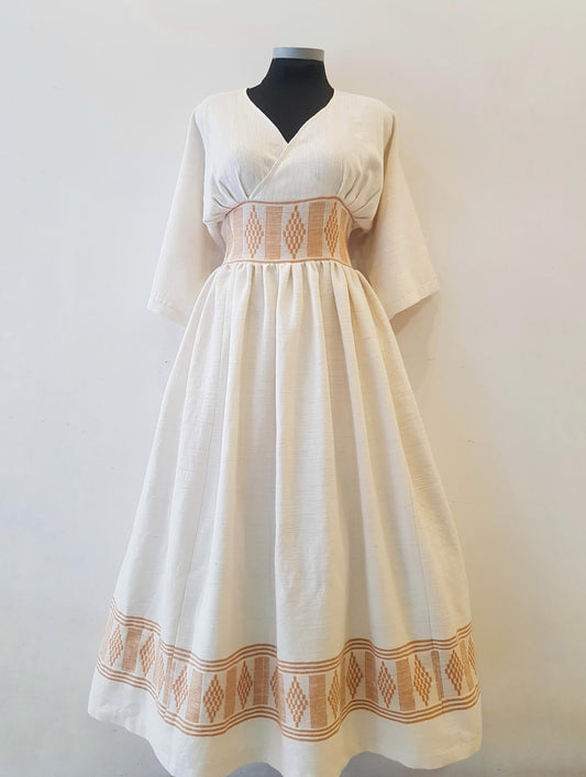 An off-white linen Ethiopian outfit  with orange geometric embroidery, displayed on a black mannequin torso against a plain light background.