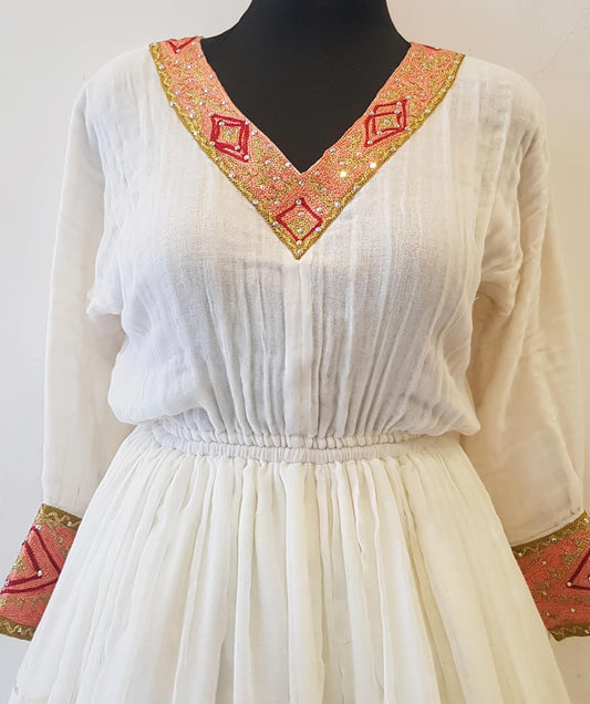 A white long-sleeve Ethiopian outfit  displayed on a black mannequin torso, featuring a V-neckline with pink and gold embroidered geometric patterns and matching embroidered cuffs.