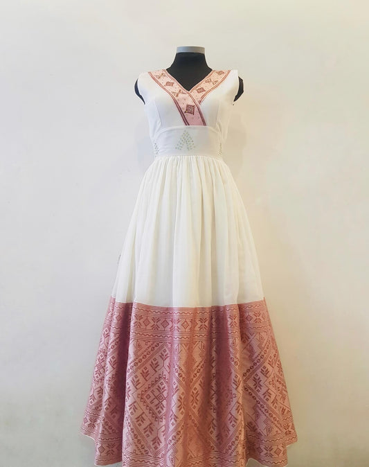 A sleeveless white maxi Pink  Ethiopian Outfit with a pink patterned border and matching pink embroidered details on the neckline, displayed on a black dress form against a plain off-white wall.