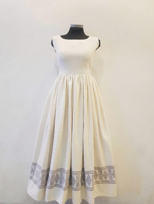 An off-white sleeveless Ethiopian outfit  with a gathered waist and a decorative border pattern near the hem, displayed on a black dress form against a plain light background.