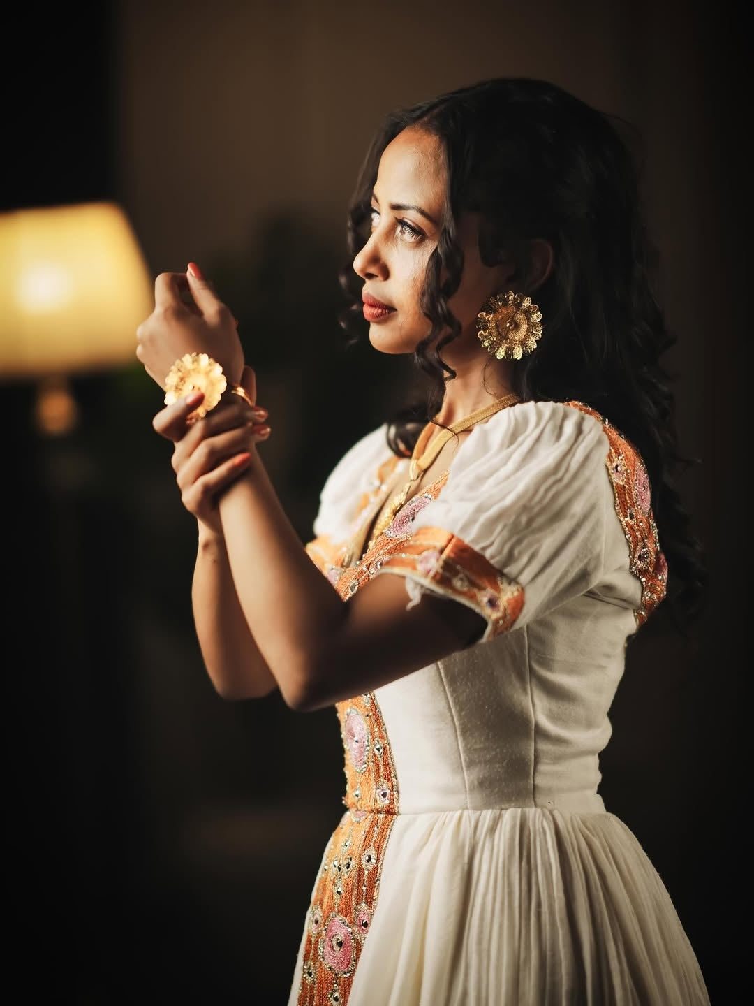 Woman in traditional attire holding a flower against a dark background