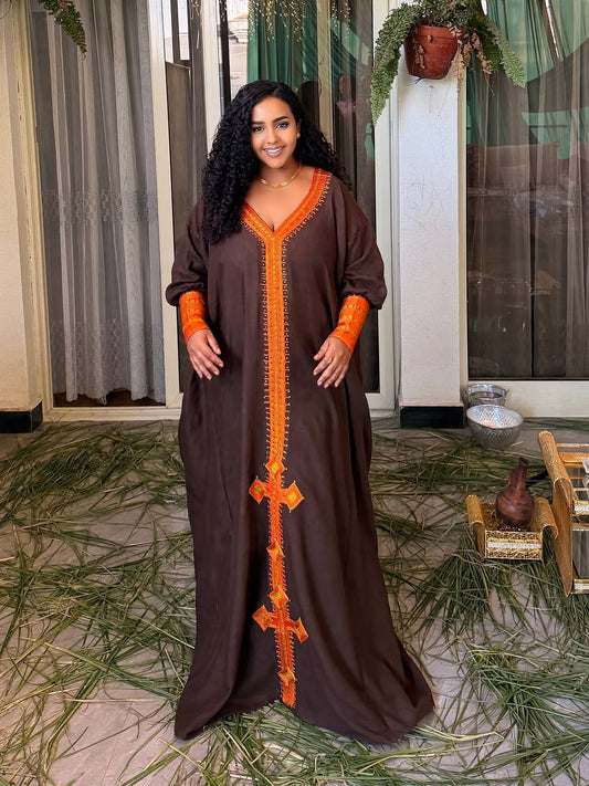 Woman wearing a long brown Habesha Dress with orange accents in an indoor setting.