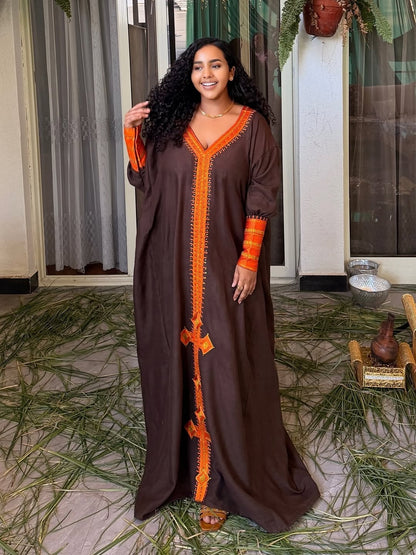 Woman wearing a brown Habesha Dress with orange accents in an indoor setting.