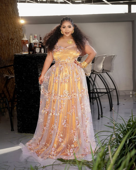 Woman in a gold evening Habesha shiffon with floral details in an indoor setting.