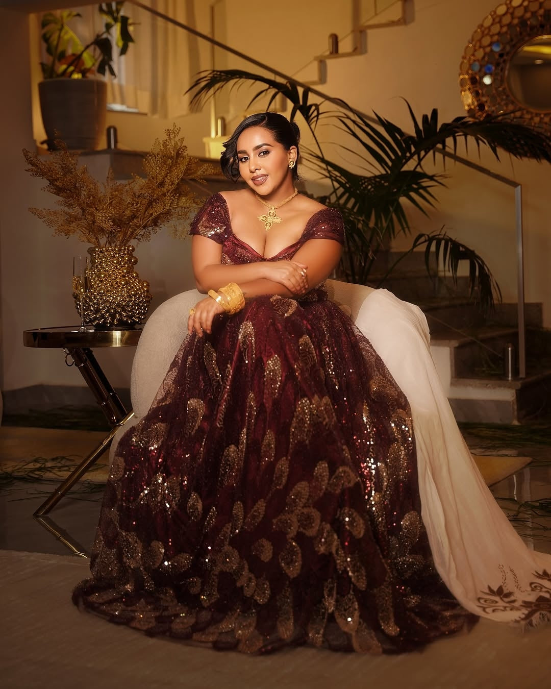 Woman in a burgundy evening habesha chiffion  with gold detailing sitting on a staircase.