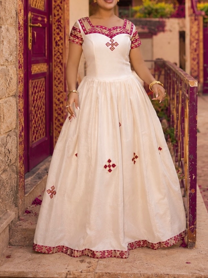 Woman wearing a white and red embroidered dress standing in front of a decorative door.