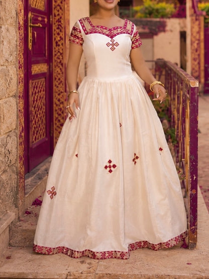 Woman wearing a white and red embroidered dress standing in front of a decorative door.