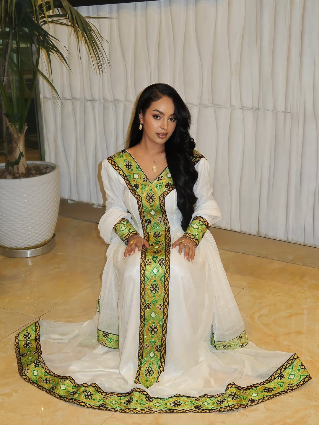 Woman in a white and green habesha dress in an elegant interior setting.