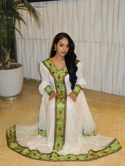 Woman in a white and green habesha dress in an elegant interior setting.