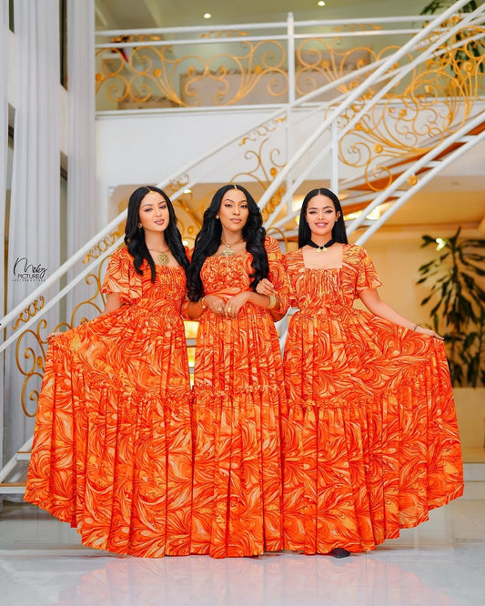 Three women in matching orange habesha chiffon standing in front of a decorative staircase.