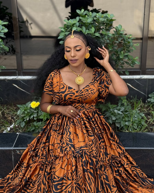 Woman wearing an orange and black patterned Habesha chiffon with gold jewelry outdoors.