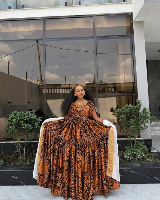 Woman in an orange and black patterned Habesha chiffon standing in front of a modern building with reflective glass windows.
