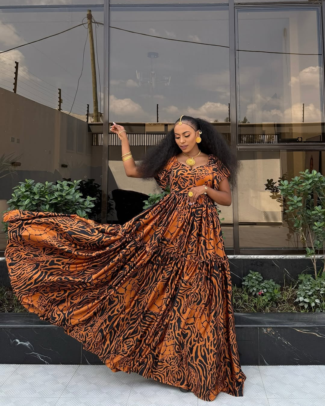 Woman in an orange and black patterned Habeshas chiffon standing outdoors with a building in the background.
