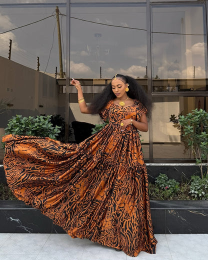 Woman in an orange and black patterned Habeshas chiffon standing outdoors with a building in the background.