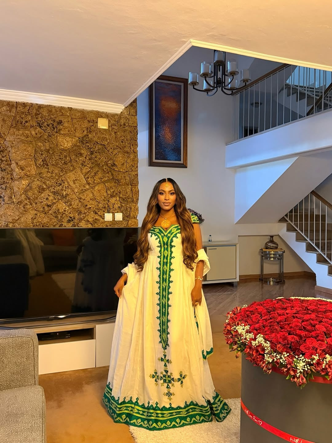 Woman in a white Green Habesha Libs  with green embroidery standing in a modern living room.