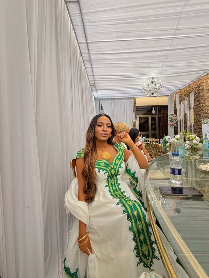 Woman in a white and green Green Habesha Libs  sitting in a decorated room with chandeliers and floral arrangements.