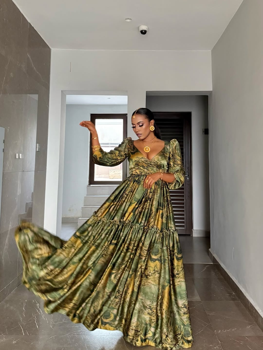 Woman in a green and gold Green Flowing Habesha Shiffon Dress standing in a modern hallway.