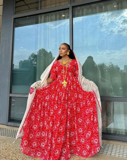 Woman in a red and white patterned Red shiffon Habesha Dress with Netela standing in front of a glass building.