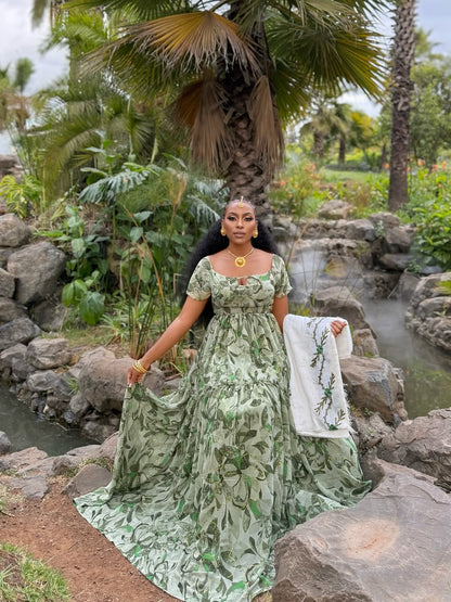 Woman in a green floral Shiffion dress standing in a garden with rocks and plants.