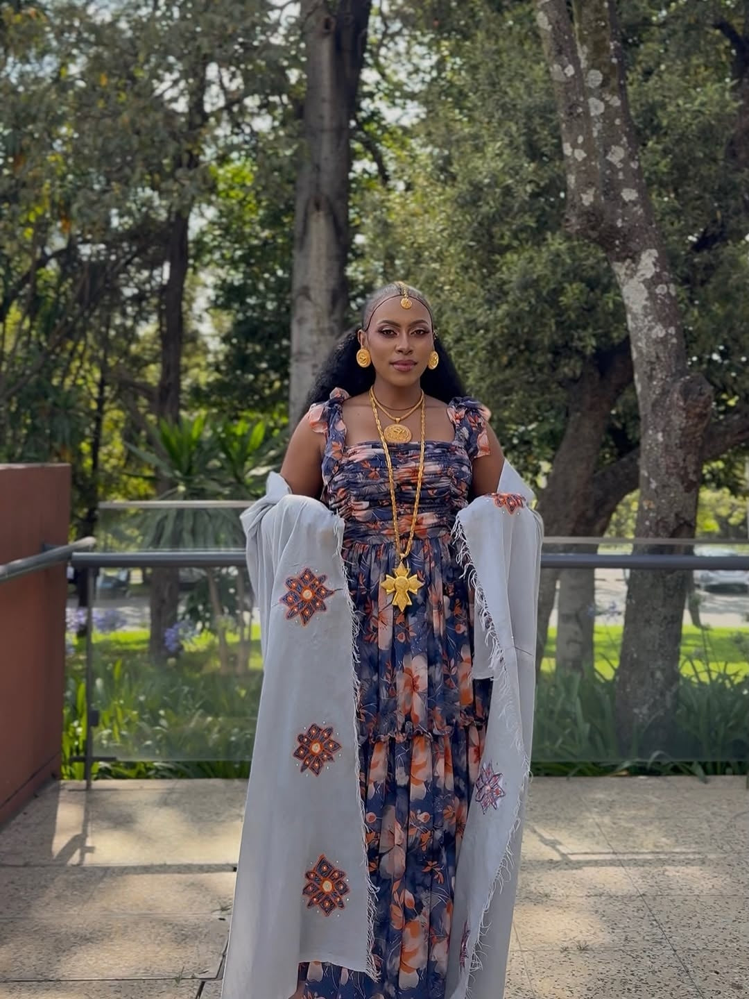 Woman in a Purple Habesha Shiffion with a white shawl standing outdoors with trees in the background