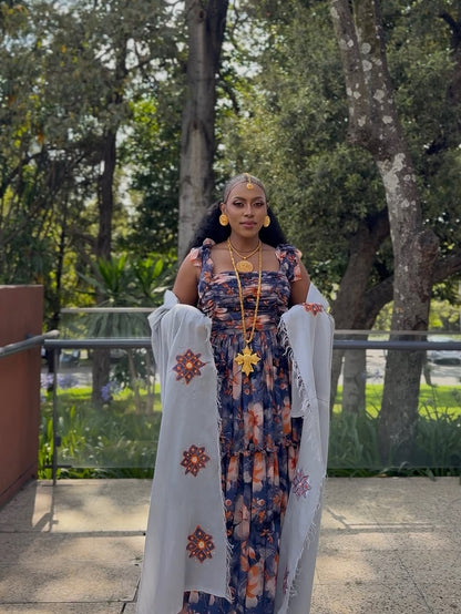 Woman in a Purple Habesha Shiffion with a white shawl standing outdoors with trees in the background