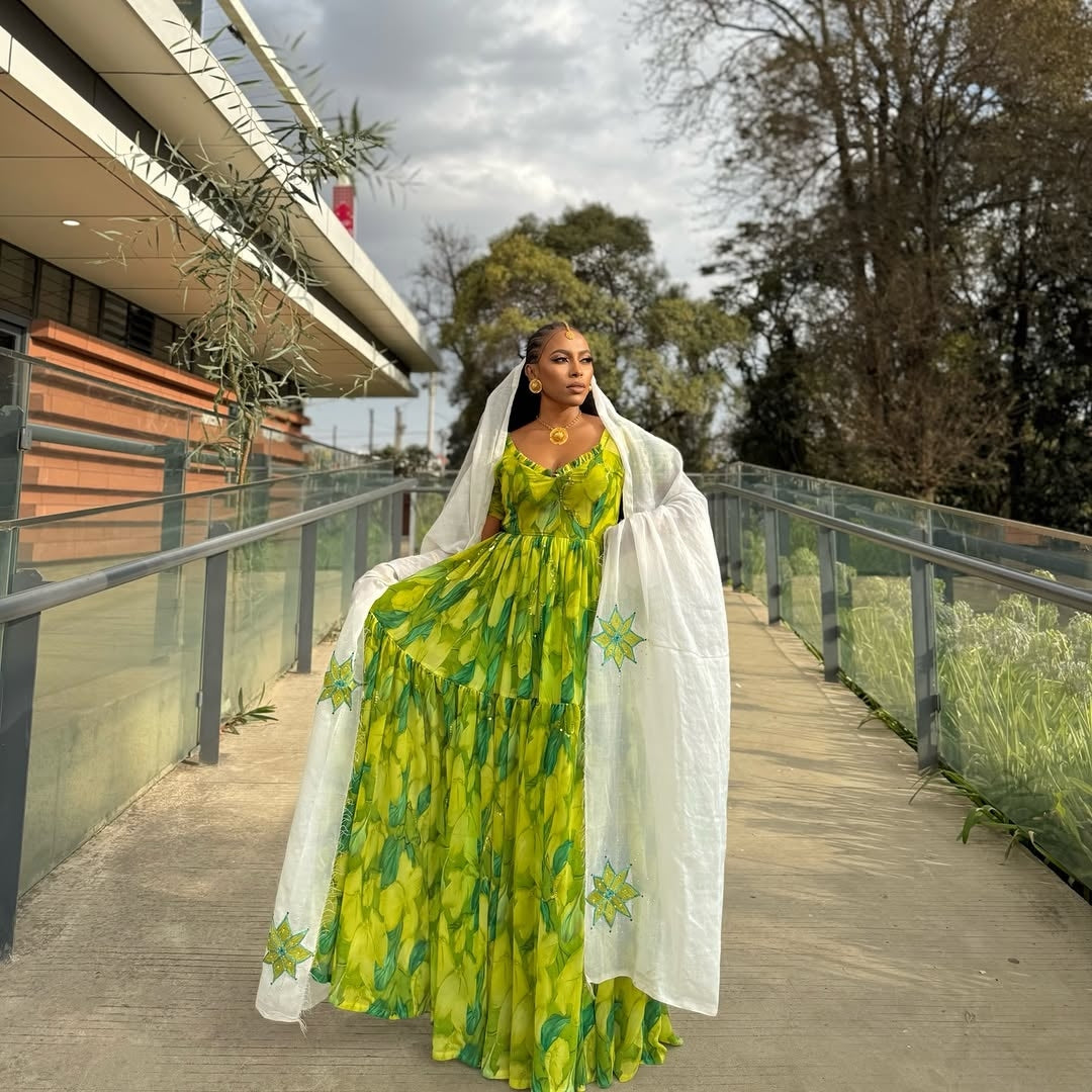 Woman in a Green Habesha Shiffion with a white shawl standing on a wooden deck with trees in the background