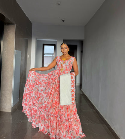 ​A woman modeling a modern pink and coral floral chiffon Habesha dress with a matching white netela scarf featuring orange traditional embroidery.