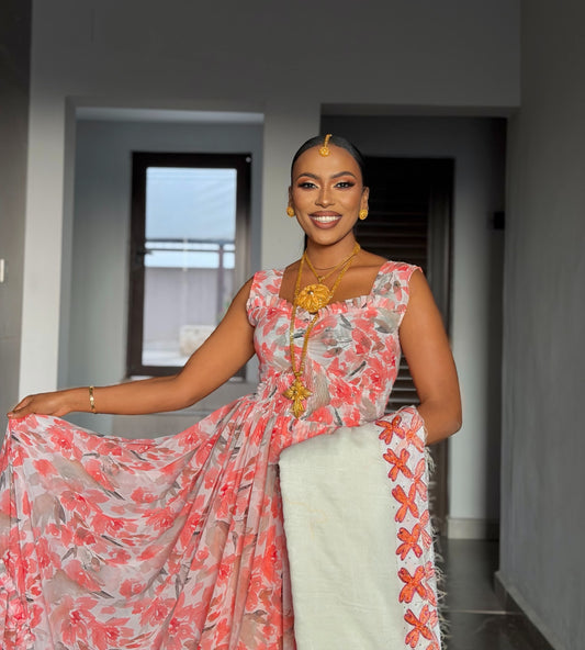 ​A woman modeling a modern pink and coral floral chiffon Habesha dress with a matching white netela scarf featuring orange traditional embroidery.