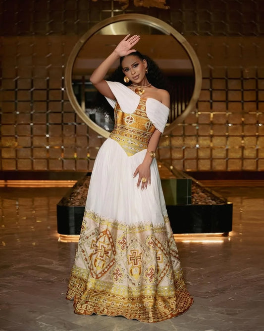 Woman in a gold and white traditional Gold Habesha Kemis posing in front of a decorative mirror.