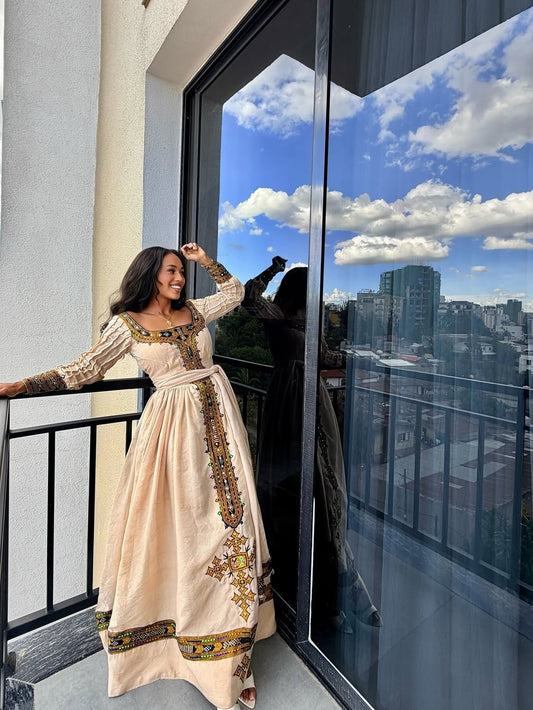 Woman in a beige embroidered Habesha Dress  standing on a balcony with a cityscape view.