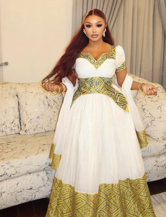 Woman in a white and green traditional Ethiopian traditional dress sitting on a patterned couch.