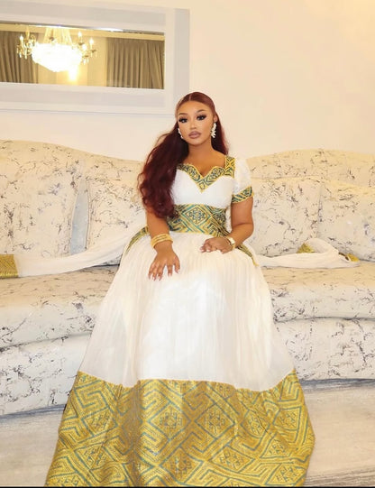 Woman in a white and green Ethiopian traditional dress sitting on a couch.