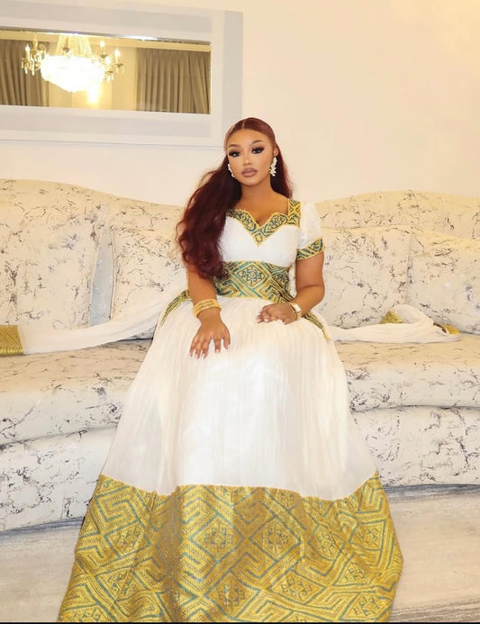 Woman in a white and green Ethiopian traditional dress sitting on a couch.