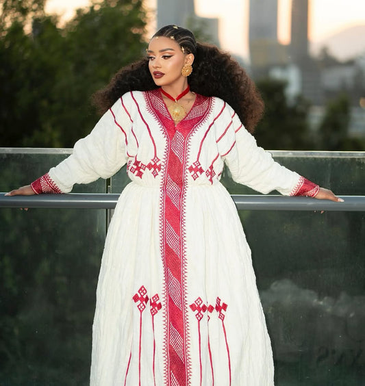 Woman in a white and red embroidered Ethiopian Dress standing on a rooftop with cityscape in the background