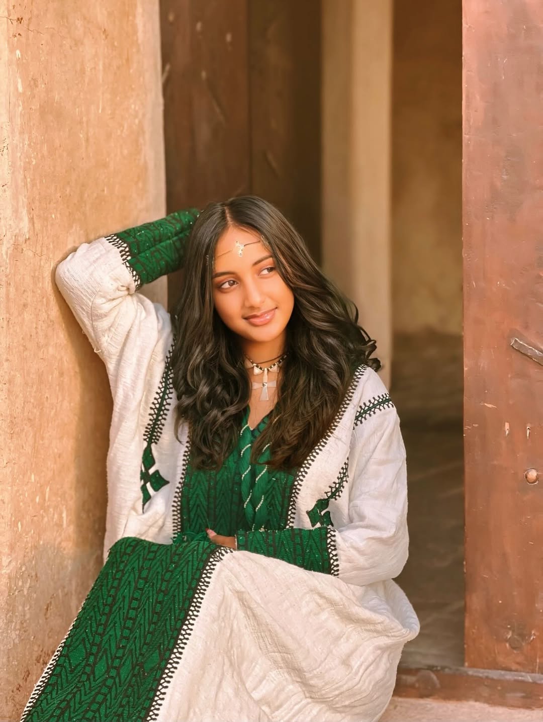 Woman in a green and white traditional Ethiopian dress sitting against a textured wall.