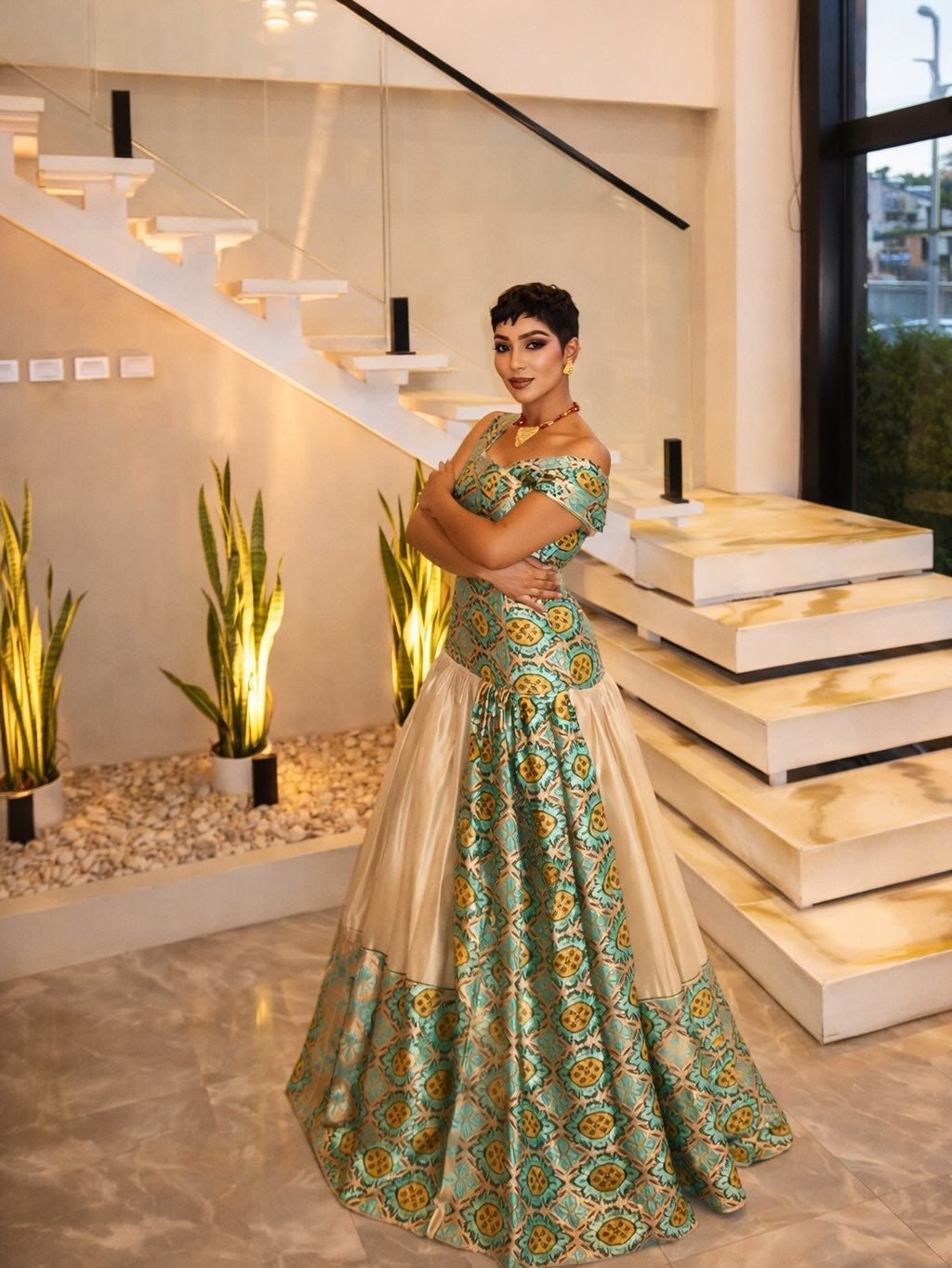 Woman in a green and gold traditional Habesha Libs standing in a modern indoor setting with stairs and plants.