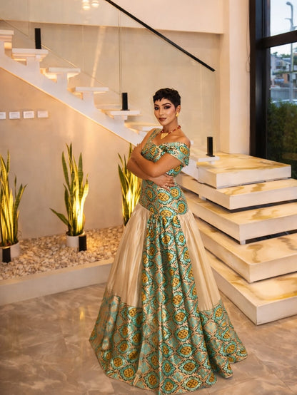 Woman in a green and gold traditional Habesha Libs standing in a modern indoor setting with stairs and plants.