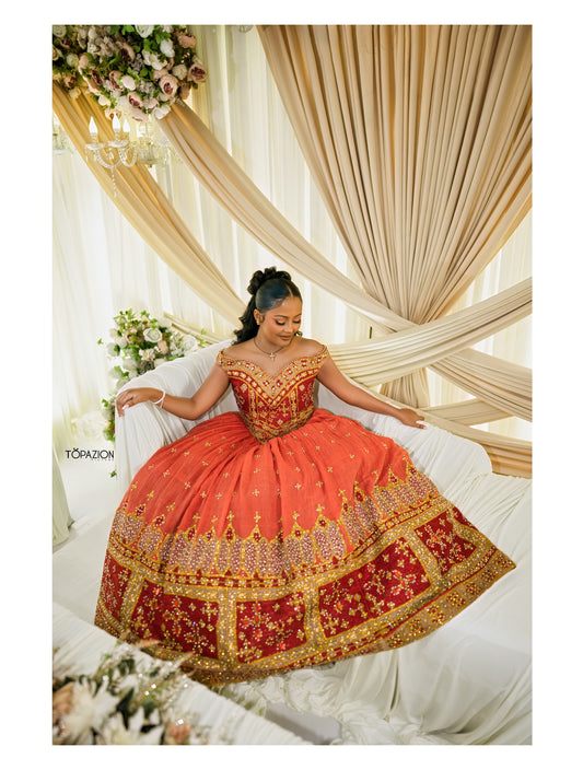 A woman wearing a voluminous peach and red embroidered traditional Habesha Wedding Dress  with gold detailing, seated on a white draped sofa in an ornate decorated event space.