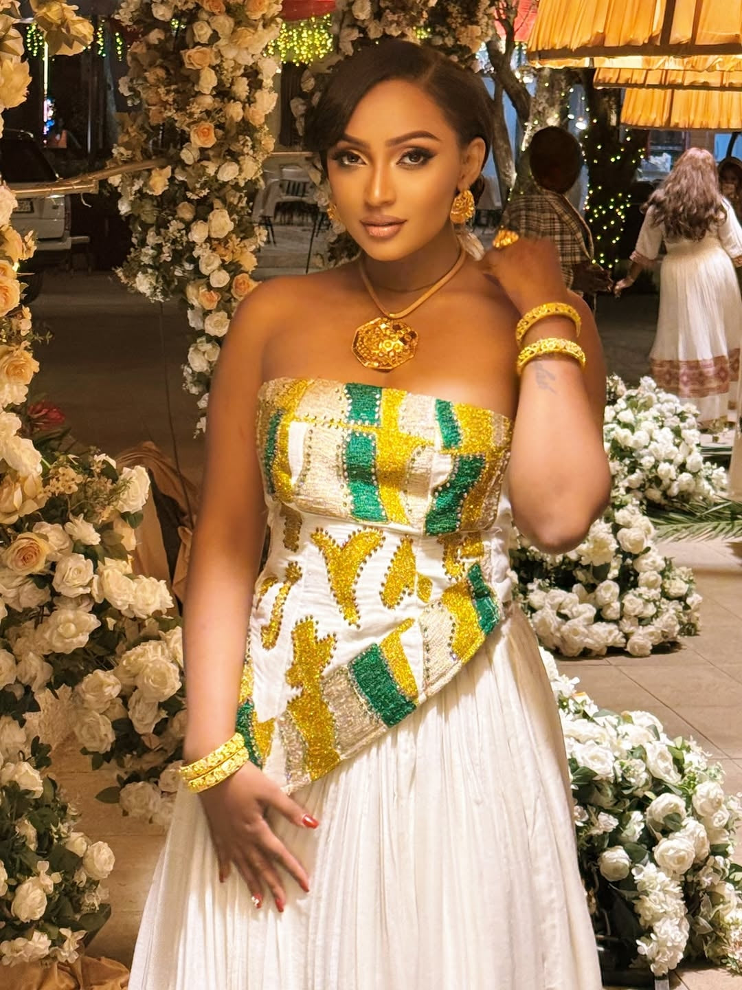 Woman in a decorated indoor setting wearing a colorful Habesha Dress.