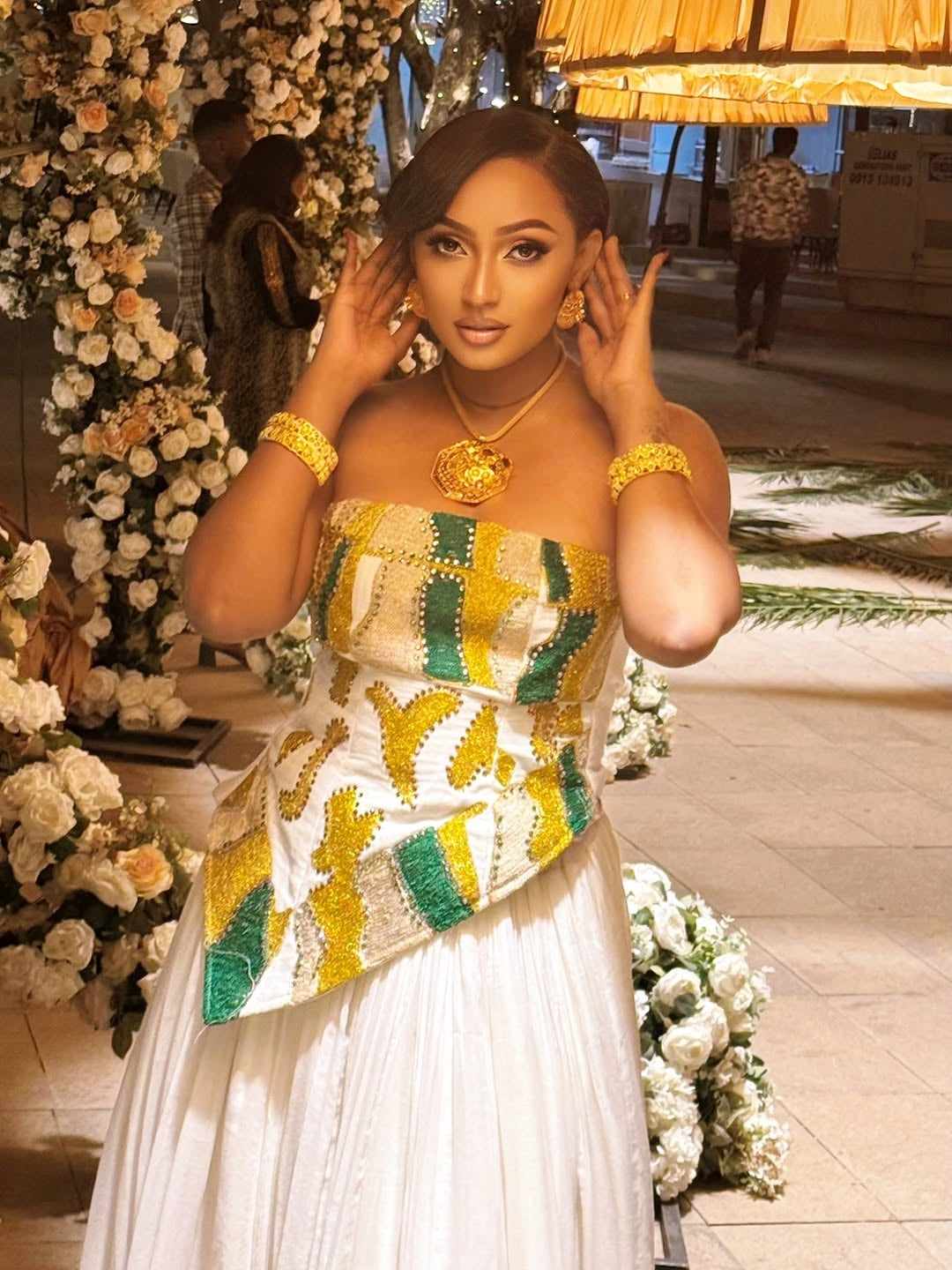 Woman in a colorful Habesha Dress with floral decorations and people in the background
